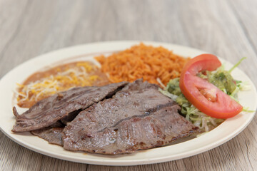 Carne asada grilled steak served on a plate with rice, and beans for a very hearty Mexican meal