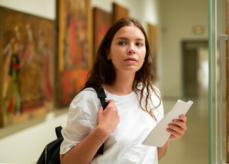 Portrait of a focused girl standing in the museum hall next to an exhibit located in a glass...