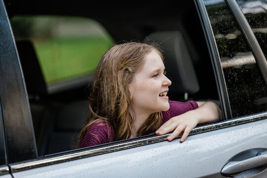 Little Caucasian Girl With Freckles And A Purple Shirt Looking Out Of A Car Window