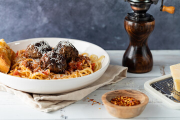 A dish of spaghetti and meatballs served with parmesan cheese and chilli pepper flakes, ready for eating.