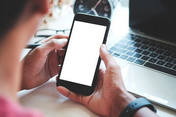 View over shoulder man sitting in front of computer laptop and using smart phone.