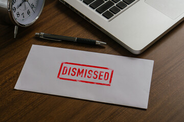 Dismissed text on paper envelope to dismiss the employee while being handed out a resignation envelope to the employee.Pen,desk clock and laptop On Wooden Desk In A Courtroom.