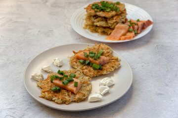 Potato pancakes with slices of lightly salted salmon with cottage cheese and green onions on plates on a gray background