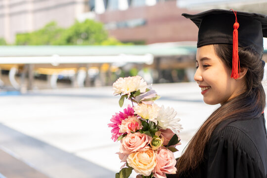 A young woman graduating in a graduation gown is blessed with a bouquet of flowers.