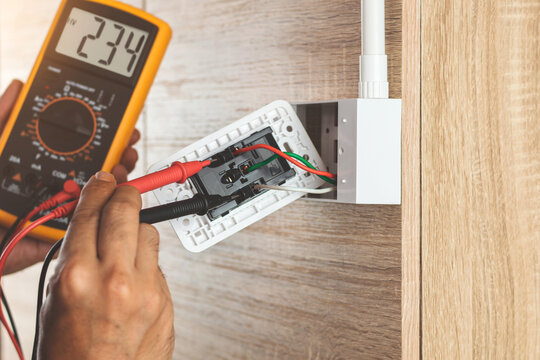 Remove the power electric plug socket from the outlet box on the wooden wall to measure the voltage with a digital meter.