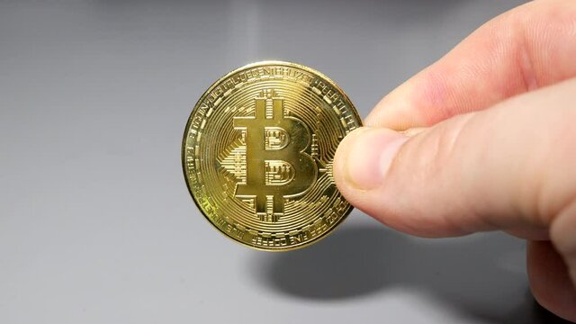 Gold bitcoin coin held between fingers in hand on gey table