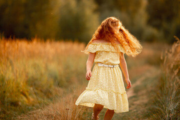 ginger baby girl 8-10 years old in yellow dress on summer fall nature background. Childhood lifestyle concept,the character, behavior of children. Having fun, fooling around, spinning, flying red hair