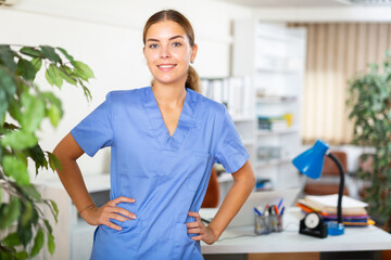 Young female doctor in surgical scrubs standing in hall of clinic.