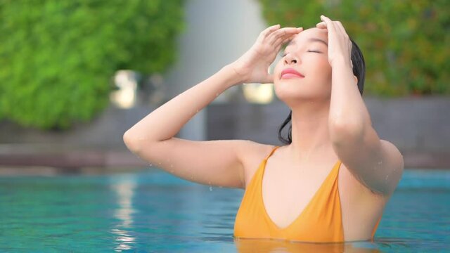 Beautiful asian woman in swimming pool touching her wet hair close up full frame slow motion