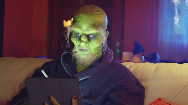 Green monster using smartphone sitting on couch