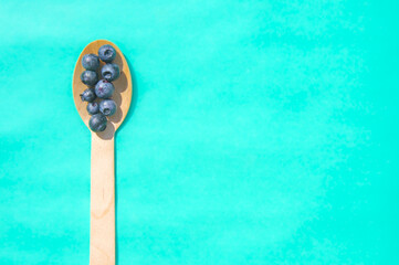 Flat lay of recycled spoon and juicy fresh blueberries on color table. Space for text. Isolated ripe sweet bilberry fruits in eco spoon on turquoise background. Copyspace. Healthy raw vegetarian food 