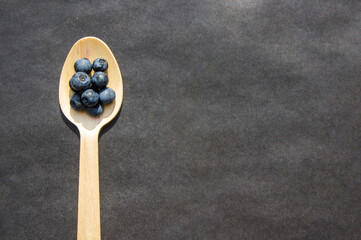 Flat lay of recycled spoon and juicy fresh blueberries on rough table. Space for text. Isolated ripe sweet bilberry fruits in eco spoon on black background. Copyspace. Healthy raw vegetarian food 