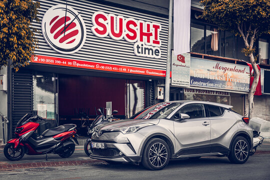 Alanya, Turkey &ndash; April 12 2021:  silver Toyota C-HR  and  motorbike parked  on the street in city against the backdrop of a   sushi restaurant, buildung,  shops, trees