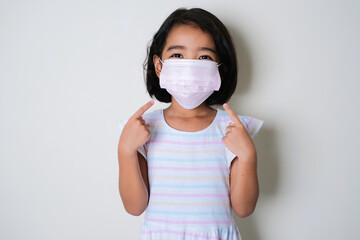 Asian little girl wearing protective medical mask and her fingers pointing on it