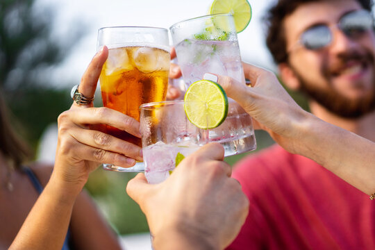 Group of young friends toasting outdoors. Focus on glasses, blurred faces.