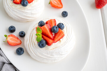 Pavlova meringue cake with whipped cream and fresh berries on top on a plate on a white wooden background. Summer dessert. Copy space, top view.