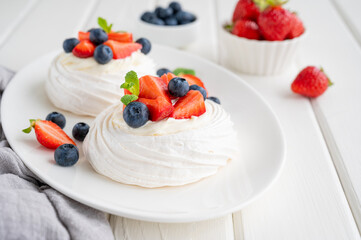 Pavlova meringue cake with whipped cream and fresh berries on top on a plate on a white wooden background. Summer dessert. Copy space.