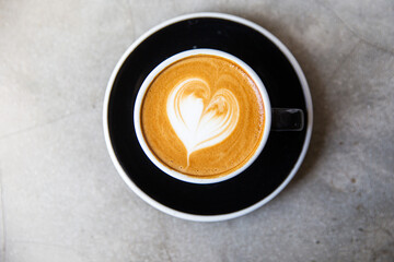 Black cup of cappuccino with latte art of heart shape on saucer on concrete background.