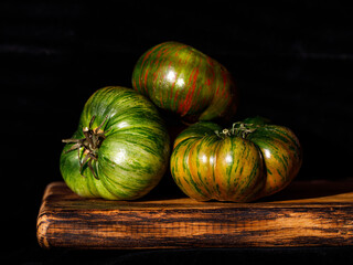 still life food composition of three green striped chocolate stripes tomatos om wooden cut board on...