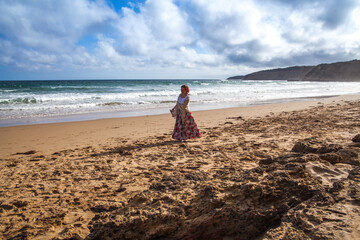 The girl stands on the beach and looks towards the sea on a summer day.