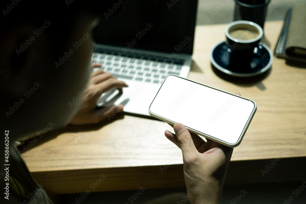 Poster close up view man holding mobile and working on computer laptop.