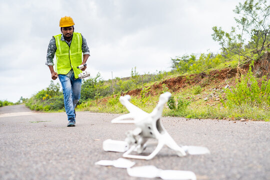 Worried drone operator running in hurry near crashed drone on road - concept of UAV damage or accident while flying.