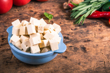 Diced tofu in a cup with vegetables for salad on the table.
