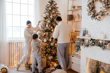 Happy beautiful family with a small son decorate the christmas tree in the house - 458667251