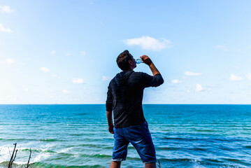 Silhouette middle age man drinking water on a sea beach light blue sky clouds. outdoors summer background.Back view.