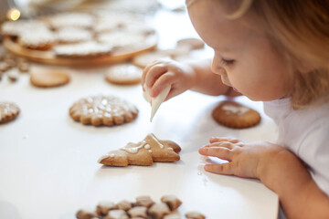 children decorate Christmas gingerbread at home. A boy and a girl paint with cornets with sugar...