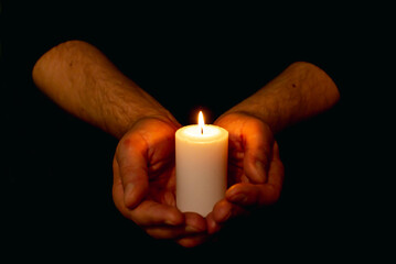 Hands holding burning candle in dark like a heart.Selective focus,black background.