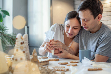 Beautiful man and woman decorate Christmas gingerbread. Two people draw a heart on the cookie. Stylish home kitchen