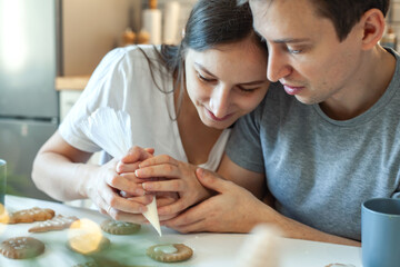 Beautiful man and woman decorate Christmas gingerbread. Two people draw a heart on the cookie. Stylish home kitchen