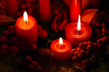 Candlelight in the dark. The atmosphere of Halloween. Autumn orange pumpkins, red berries, fallen oak leaves and burning candles