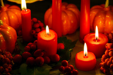 Candlelight in the dark. Halloween decor. Autumn orange pumpkins, red berries, fallen oak leaves and burning candles