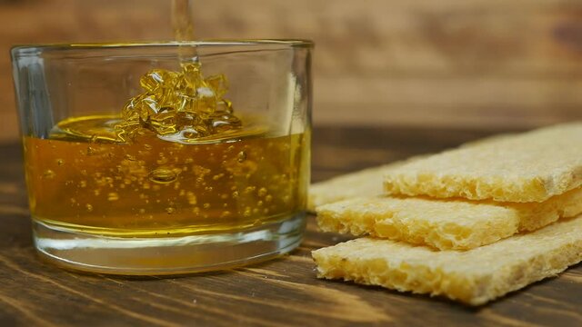 Natural flower honey of a yellow hue is poured into a glass container close to a wooden table on a wooden table crunchy rectangular bread. The concept of a healthy breakfast without fat. Dolly shot