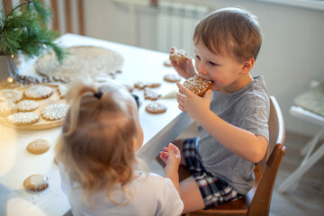Boy and girl decorate and eating Christmas gingerbread at home. A boy and a girl paint with cornets...