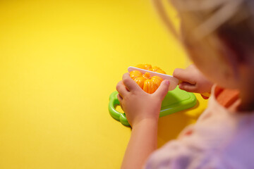 A child cuts a toy pepper on a yellow background with a toy knife