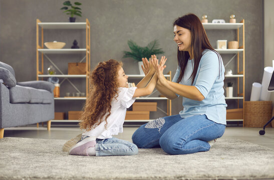 Young woman and her daughter enjoy spending time at home playing a game of clapping. Loving family sitting on the floor in the living room and playing clapping each other. Family concept.