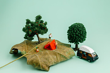 Camping in nature on a dry autumn leaf with a small tent, miniature people, two trees and a camping...