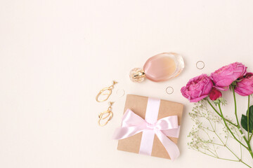 Layout of flowers bouquet, gift with tied bow, feminine accessories on a beige background. Tenderness female composition with copy space.