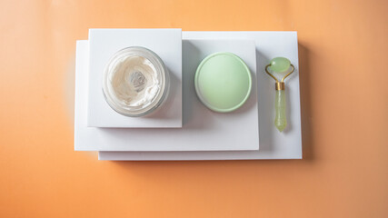 Three podiums at beige background with gua sha roller and natural crem for holistic eauty and skin care concept.