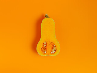 A half of nutmeg pumpkin or gourd isolated on vibrant orange background. Minimal fresh, raw cooking ingredient. Creative Halloween or Thanksgiving concept. Fall season vegetable backdrop. Flat lay.