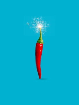 Single red hot chili pepper with fire sparkler isolated on a vibrant blue background. Creative spicy vegetable food concept. New Year or Christmas party decoration. Fashion minimal art.
