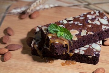 Chocolate spongy brownie cakes with almonds and melted syrup caramel topping on a stack and mints...