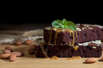 Chocolate spongy brownie cakes with almonds and melted syrup caramel topping on a stack and mints on top. dessert style.