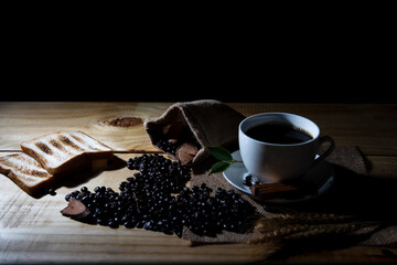 Black hot coffee cup and beans with breads on wooden table at cafe. Dark scene and use for banner