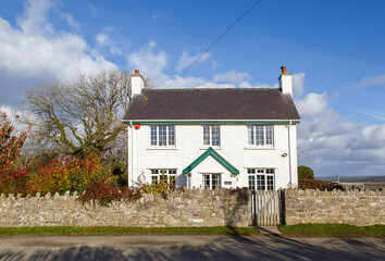 Traditional white painted country cottage with stone walls and blue sky background - UK