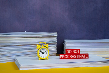 Business concept. Layout of alarm clock, stack of papers and wooden block with text Do Not Procrastinate