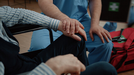 Close up of hands of nurse and senior patient at medical visit in nursing home. Medical assistant giving support and comforting old man in wheelchair. Specialist helping disabled person